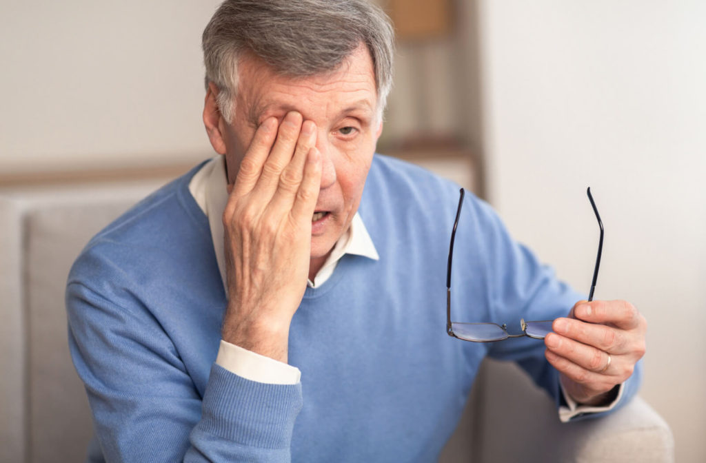 A senior man sitting on a sofa is rubbing her eyes due to blurred vision from glaucoma