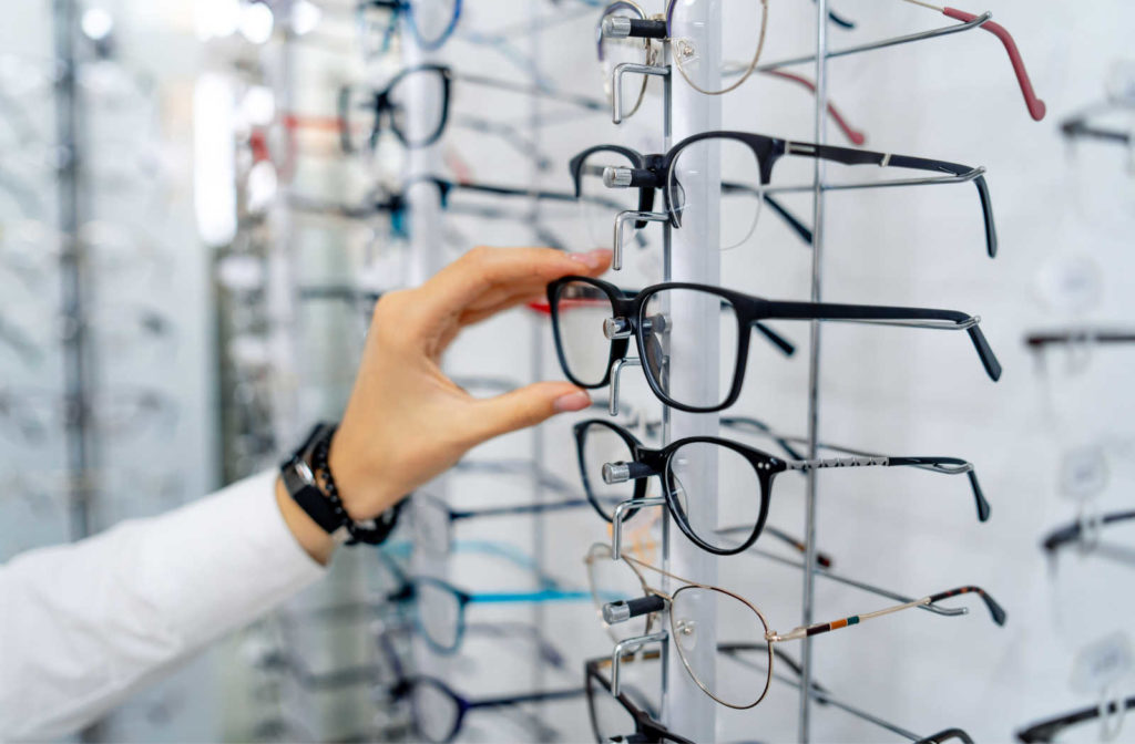 A hand reaching out to try on a pair of eyeglasses chosen from an eyeglass display after an eye exam