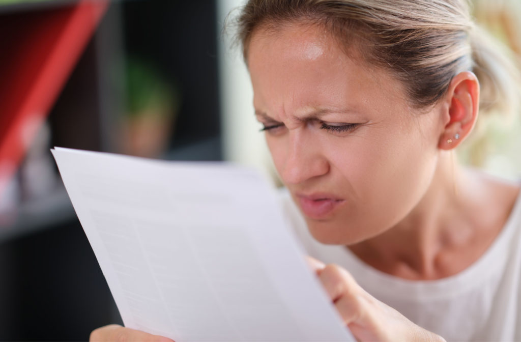 A woman squinting and leaning closer towards a document to read its content better.