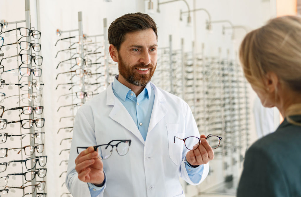 An optometrist presenting two pairs of glasses to his patient.