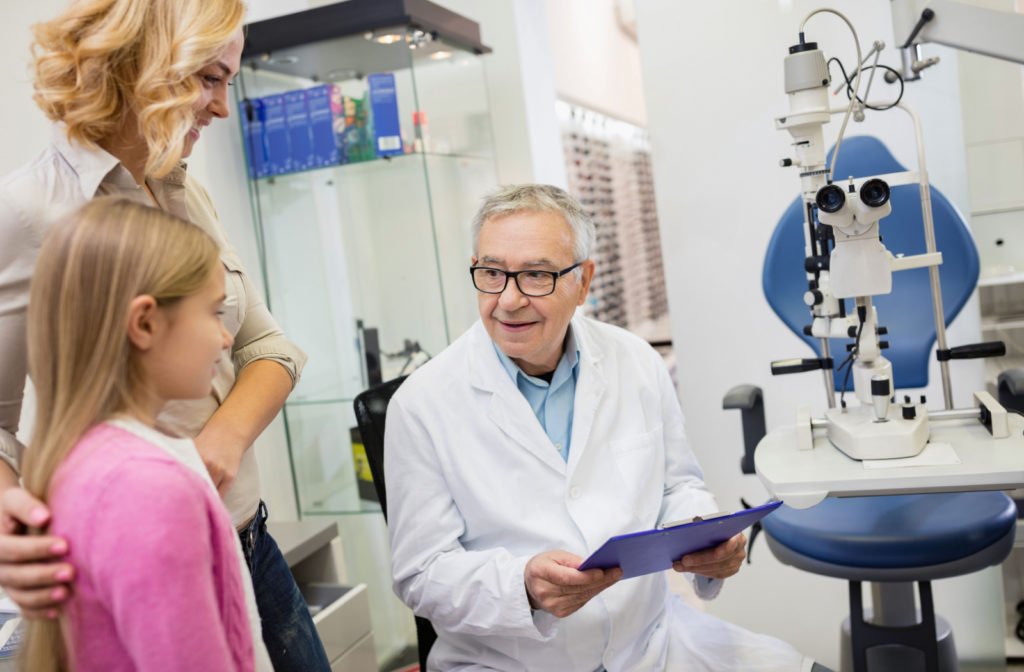 An eye doctor holding a clipboard while talking to his young patient.