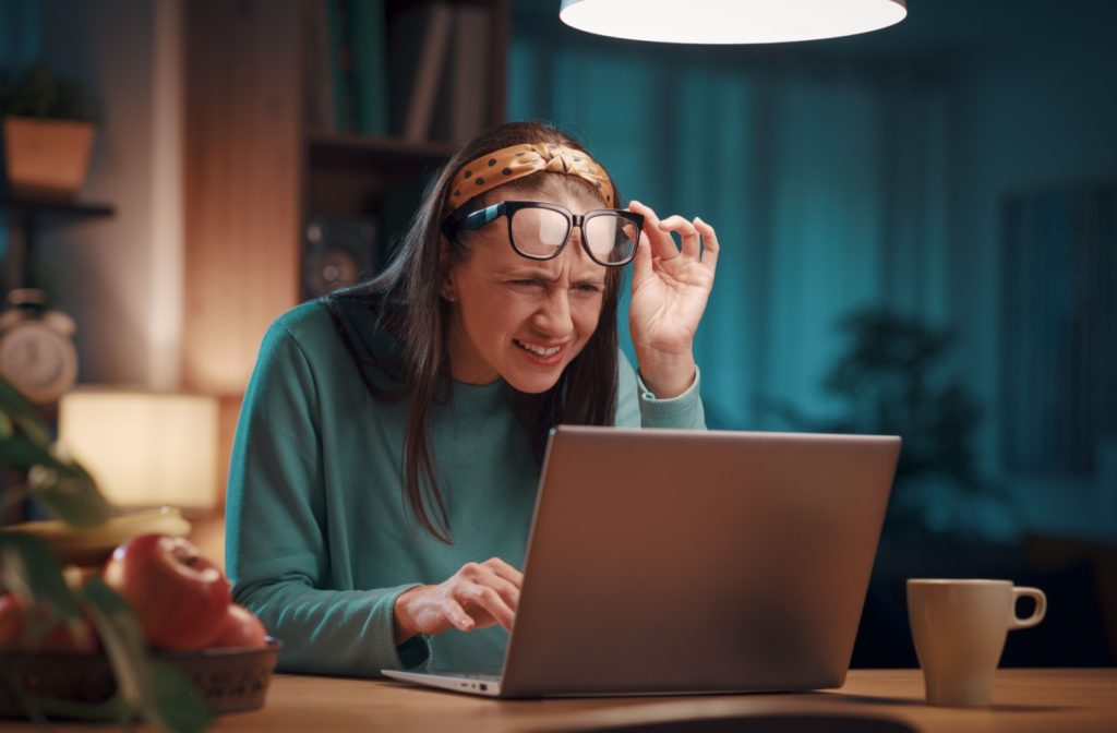 A woman squinting and leaning in closer to her laptop to see its contents clearly.