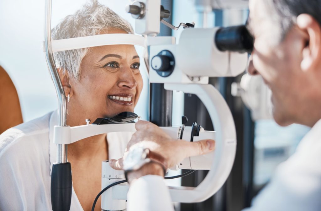 An optometrist examines a smiling older female patient's eyes during a comprehensive eye exam.