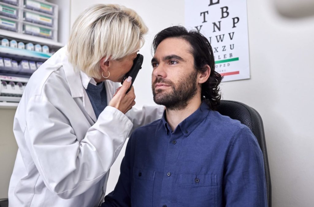 A male patient staring forwards during an eye exam while an optometrist examines a chalazion on his right eye.