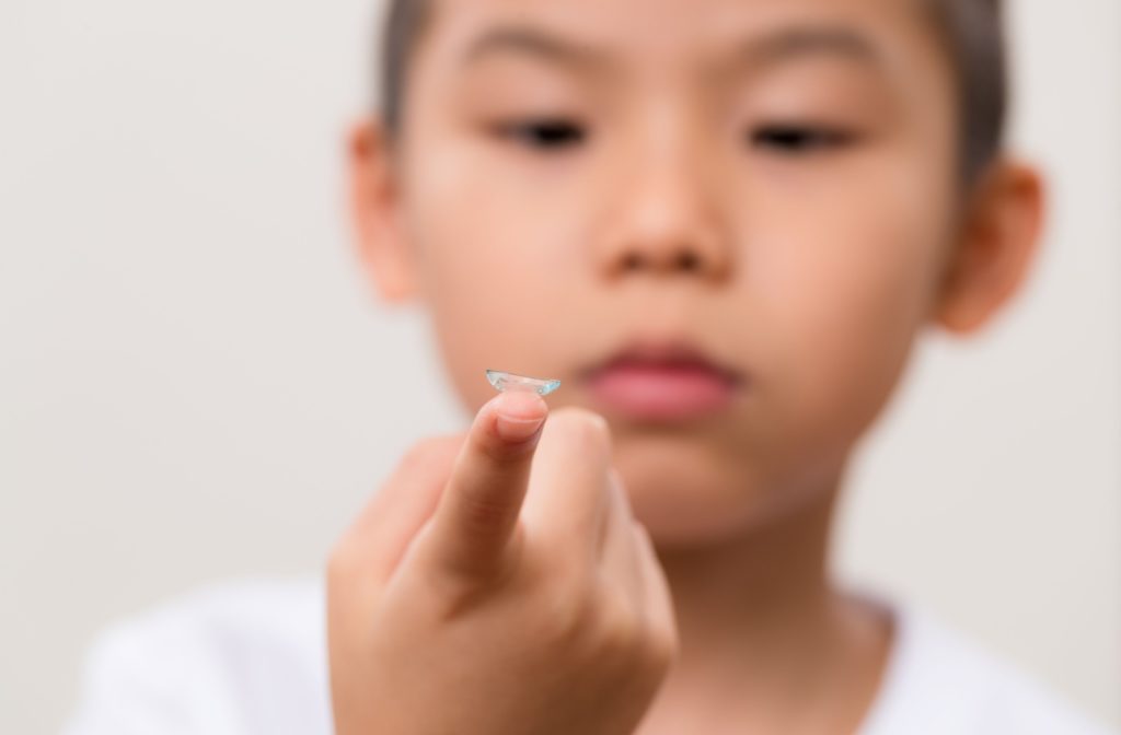 A young child holds a contact lens on one finger in front of their face