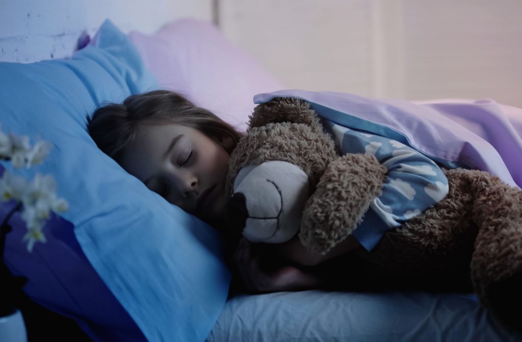 A young child asleep in bed with Ortho-K lenses in, cuddling a teddy bear close to their chest