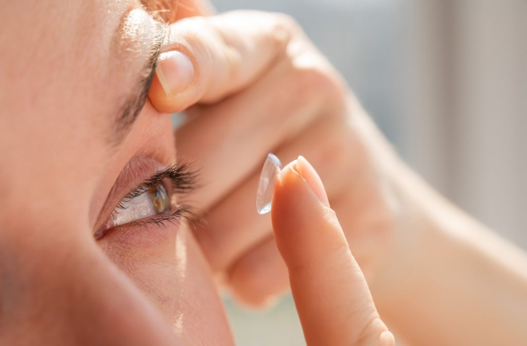 A close-up image of a person putting a contact lens in their left eye.