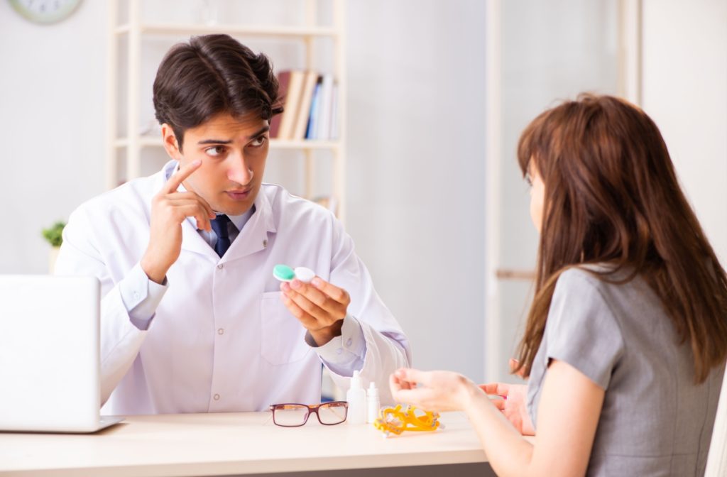 An eye doctor holding a contact lens case and discussing contact lenses with a patient.