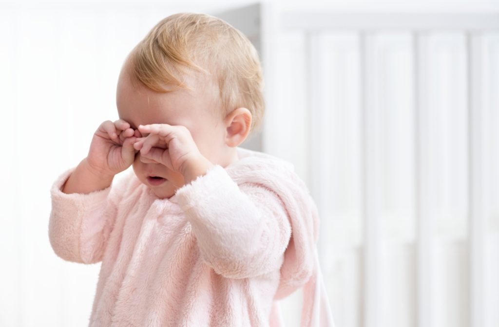 A frustrated toddler rubs their irritated eyes.