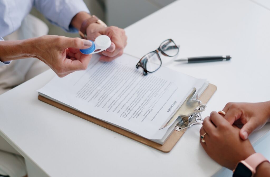 An optometrist holds out a contact lens case to their patient while explaining proper care.