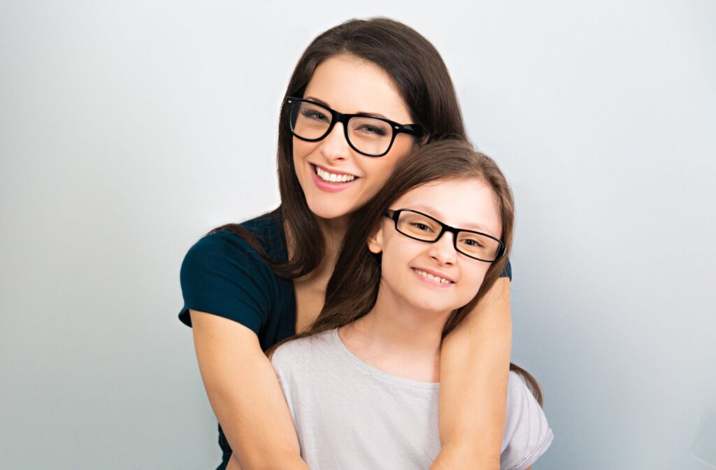 A parent and their child, both wearing similar glasses, stand together.