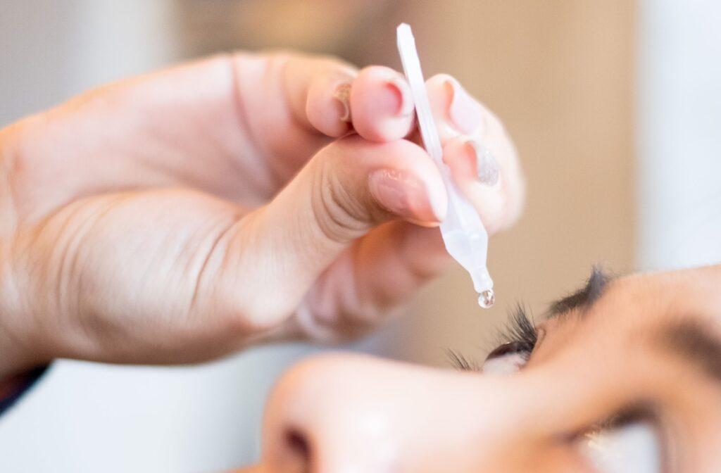 Close-up of a woman squeezing eye drops into eye while tilting head back.