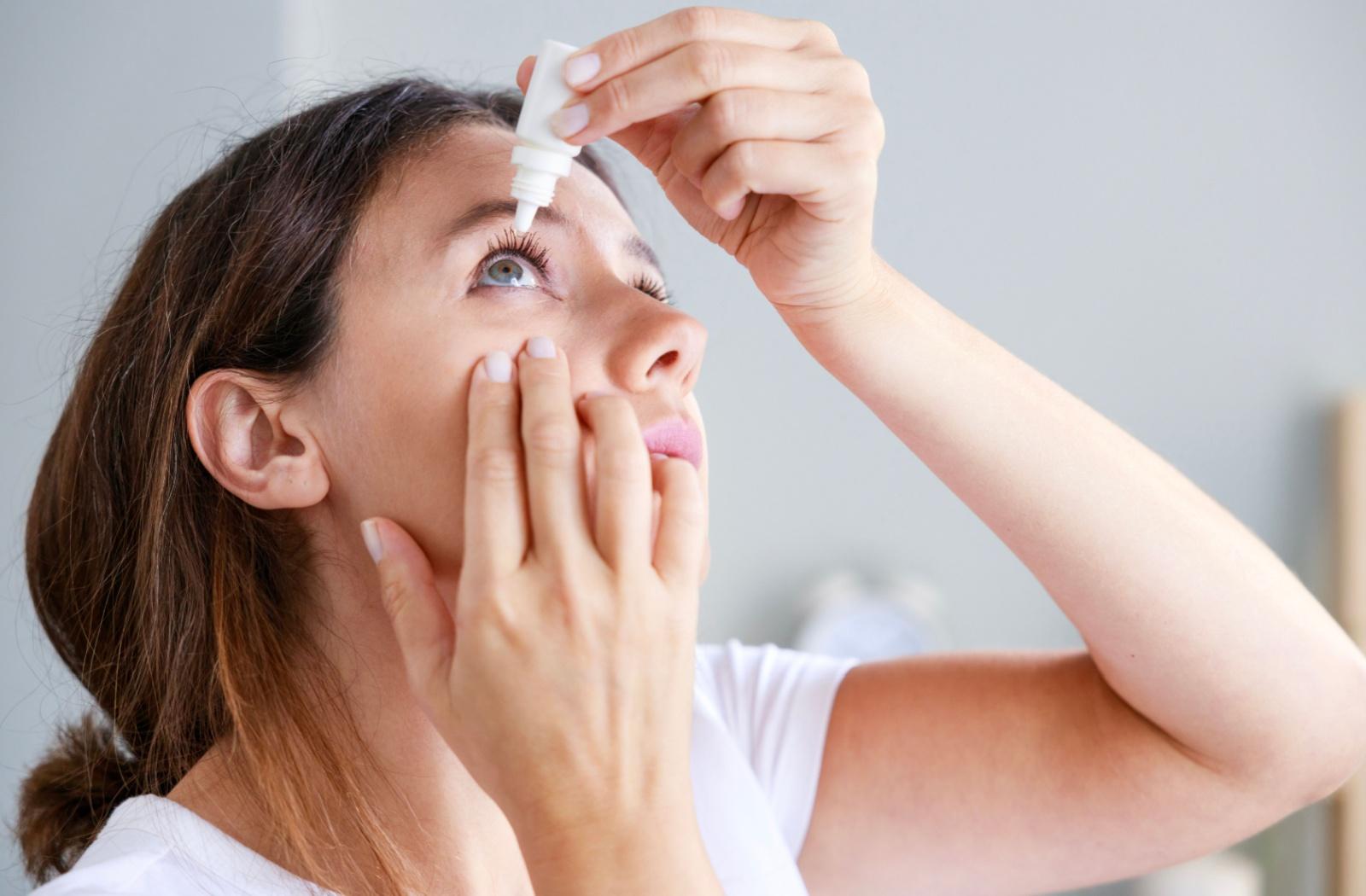 A person inserting eye drops to reduce the irritation and symptom of a burning feeling.